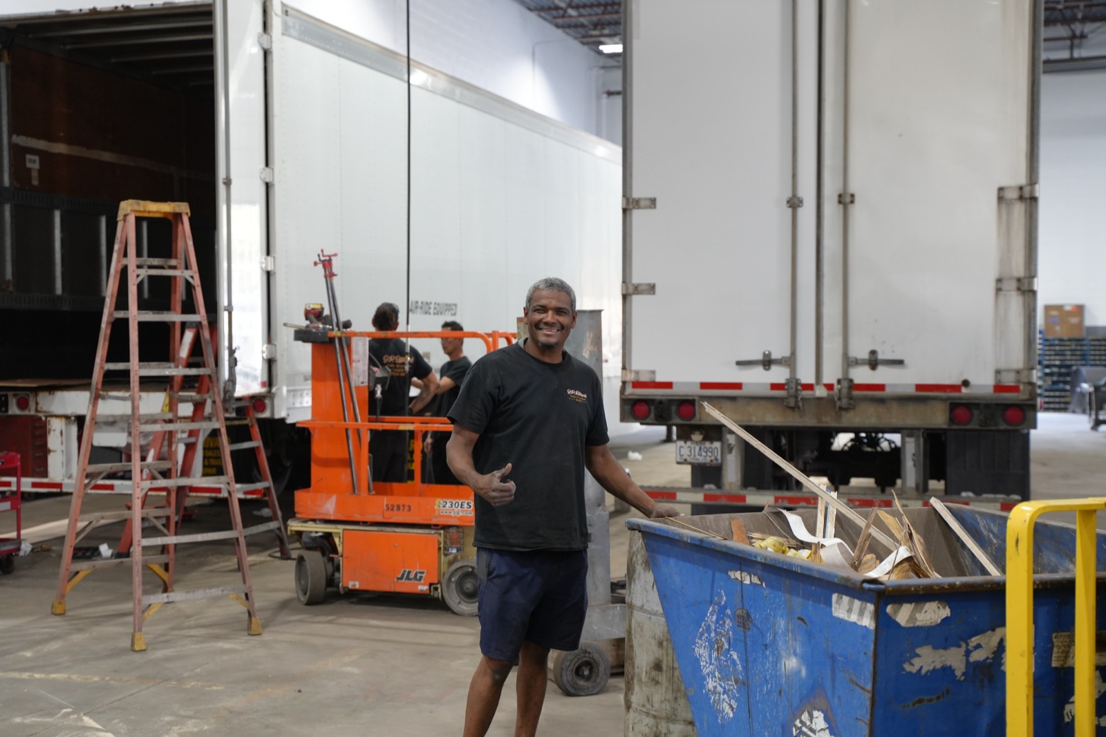 JP Rivard service technician waving in the repair shop, trailers behind him